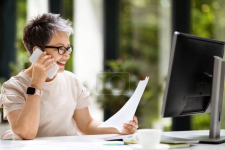 Photo for Stylish pretty middle aged woman in smart casual executive manager CEO working at modern office, sitting at workdesk in front of pc computer, talking on phone, reading papers documents - Royalty Free Image