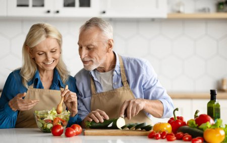 Photo for Happy senior couple preparing healthy salad together in kitchen interior, smiling mature husband and wife cooking vegetarian lunch or dinner at home, man chopping vegetables, copy space - Royalty Free Image