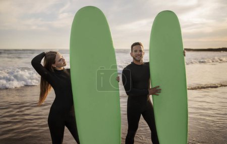 Photo for Summer Activities. Happy Young Couple Posing With Surfboards On The Beach, Cheerful Millennial Man And Woman Wearing Wetsuits Surfing Together, Enjoying Vacation And Water Sports, Copy Space - Royalty Free Image