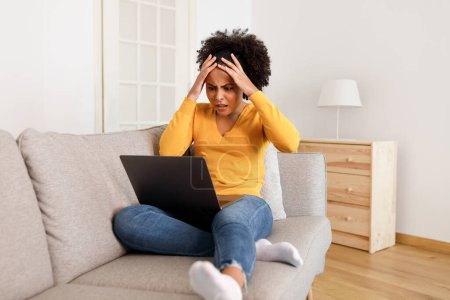 Photo for Online Work Problem. Frustrated Black Freelancer Woman Having Computer Issues Working Remotely At Laptop, Clutching Her Head in Shock Sitting on Sofa At Home. Troubles with Internet Connection - Royalty Free Image
