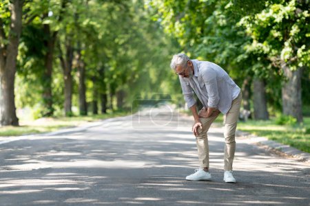Photo for Mature Man Suffering Knee Injury While Walking Outdoors In Park, Senior Gentleman Having Osteoarthritis, Standing On Path And Rubbing Painful Area, Feeling Unwell During Outside Walk, Copy Space - Royalty Free Image