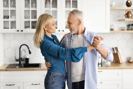 Téléchargez les photos : Heureux époux. Aimer mari et femme âgés dansant à l'intérieur de la cuisine, gai homme et femme âgés s'amusant ensemble à la maison, se tenant la main et se souriant, Espace libre - en image libre de droit