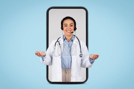 Foto de Amable médico brasileño mujer con auriculares en la pantalla del teléfono inteligente enorme gesto y sonriendo a la cámara, tener cita en línea, fondo azul, collage - Imagen libre de derechos