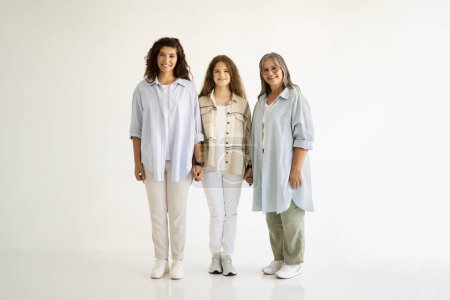 Photo for Positive caucasian old, adult and young women in casual holding hands, enjoy love and support on white wall background. Relationships grandmother, mother and daughter, ad and offer, full length - Royalty Free Image