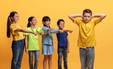 Photo for Angry cruel multiracial kids teenagers laughing and pointing at their classmate boy covering his ears with hands. School aged children bullying child. Social inequality problem. Schoolchildren baiting - Royalty Free Image