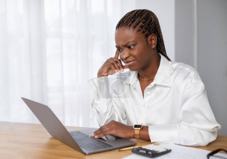 Foto de Mujer negra joven infeliz en traje formal empleado sentado en el lugar de trabajo, utilizando el ordenador portátil en la oficina, mirando a la pantalla de la computadora y tocando su cabeza, tienen dificultades en el trabajo, espacio para copiar - Imagen libre de derechos