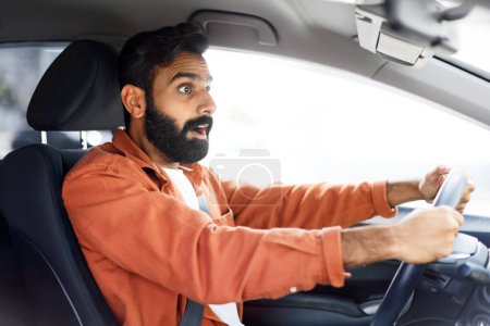 Foto de Situación de tráfico peligroso. Impresionado joven indio que conduce con riesgo de accidente de coche, sosteniendo el volante, mirando la carretera en shock, vista lateral. Problema de seguridad de los viajes en automóvil - Imagen libre de derechos