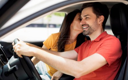 Foto de Amar a la joven mujer caucásica besando a su marido guapo feliz conduciendo coche. Alegre emocionado pareja millennial cónyuges disfrutando de viaje por carretera, pruebas de automóviles nuevos, vista lateral - Imagen libre de derechos