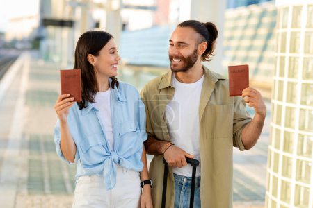 Photo for Glad millennial caucasian man and lady with suitcase show passports, enjoy trip, immigration at airport, train station. Travel together, relationships and romance, summer vacation tour - Royalty Free Image