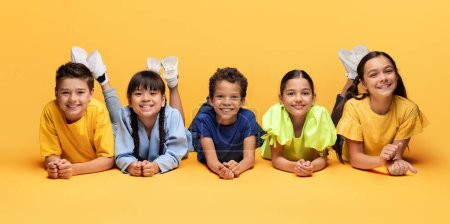 Vielfalt, Porträt glücklicher multiethnischer Kinder, die auf dem Boden liegen und gemeinsam auf gelbem Hintergrund lächeln. Glück oder aufgeregt, Gruppe von Freunden Kinder haben Spaß, genießen Spiele, Kindheitskonzept