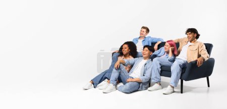 Photo for Excited diverse teen friends watching tv, sitting on sofa and floor over white studio background, looking at copy space, panorama, banner - Royalty Free Image