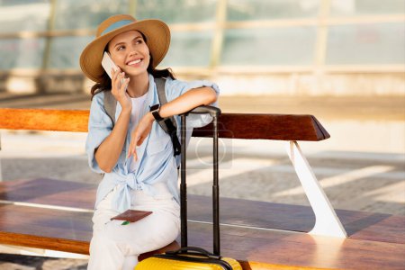 Téléchargez les photos : Heureuse jeune femme caucasienne en chapeau avec valise, passeport et billet, profiter des voyages, appeler par téléphone, regarder l'espace libre à la gare, aéroport. Communication, commérage, annonce et offre - en image libre de droit
