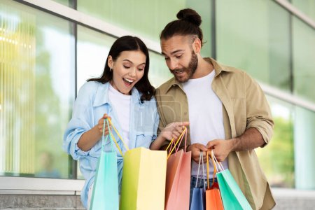 Glad shocked young european woman and man looking at bags, enjoy shopping, purchases in mall. Shopaholics, sale, discount and surprise for clients, people emotions, lifestyle
