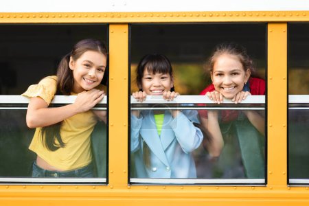 Photo for Group of teen girls peeking out of school bus window, waving and smiling at camera, cheerful female friends enjoying their trip in yellow schoolbus, transportration for pupils concept - Royalty Free Image