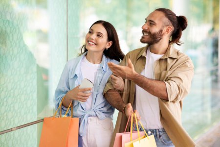 Photo for Happy surprised young european man and woman with bags enjoy shopping and free time together, look at shopwindow in mall. Sale for shopaholics in city, discount season and Black Friday - Royalty Free Image