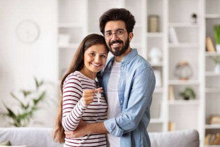 Photo for Happy young indian couple posing at new home hold house keys moving in together, loving caring husband and wife apartment owners excited relocating to own dwelling, renting, relocation concept - Royalty Free Image