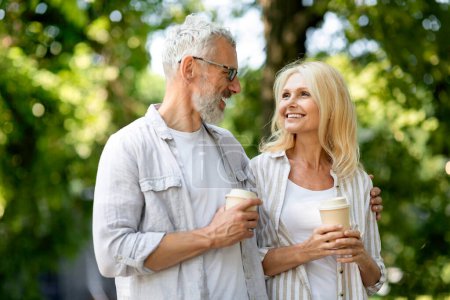 Photo for Retirement Leisure. Smiling Senior Spouses Walking Outdoors And Drinking Takeaway Coffee, Happy Mature Man And Woman Enjoying Walk In Park, Romantic Older Couple Relaxing Outside Together, Free Space - Royalty Free Image