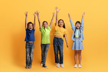 Photo for Cool cheerful diverse multiracial preteen kids having fun isolated on yellow background, raising hands up and screaming at camera. School aged boys and girls posing together, full length - Royalty Free Image