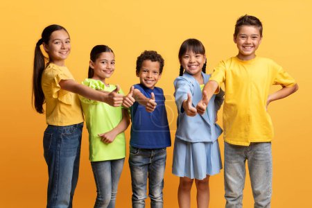 Photo for Great deal, excitng offer for kids. Happy diverse multietnic children preteen boys and girls in casual outfits showing thumb up and smiling at camera, isolated on yellow background - Royalty Free Image
