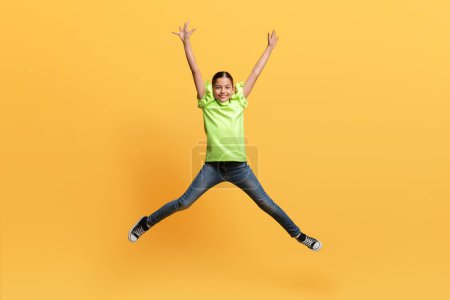 Photo for Happy pretty preteen middle eastern girl jumping with hands up in the air isolated on yellow studio background, full of energy child having fun, copy space. Kids emotions concept - Royalty Free Image