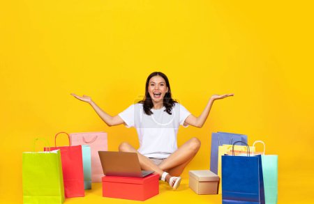 Foto de Concepto de compras en línea. Mujer joven feliz con el ordenador portátil y brillante Shopper Bolsas Sentado en el piso sobre fondo del estudio amarillo, Emocionado hermosa mujer disfrutando de ventas y descuentos, Espacio libre - Imagen libre de derechos