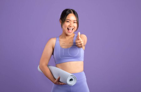 Photo for Happy young asian woman in sportswear with mat showing thumb up isolated on purple studio background, copy space. Approving, advice, recommendation for sport, yoga and body care - Royalty Free Image