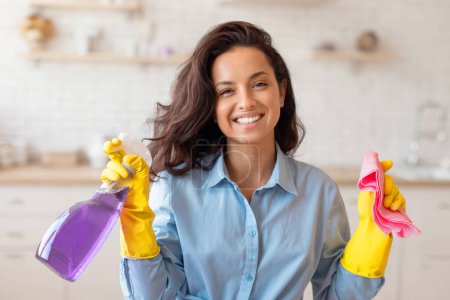 Photo for Portrait of happy maid doing cleanup in modern apartment, posing with bottle and rag and smiling at camera. Positive young woman enjoying domestic chores - Royalty Free Image