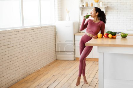 Photo for Weight Loss Nutrition. Full Length Shot Of Young Fitness Woman Enjoying Healthy Green Smoothie Drink, Standing At Modern Kitchen, Free Space For Text. Dieting And Slimming Offer Advertisement - Royalty Free Image