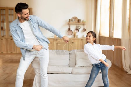 Photo for Funny Leisure Activities. Cheerful Hispanic father and preteen daughter girl moving and dancing to music indoors, having fun partying, enjoying time at home in modern living room interior - Royalty Free Image
