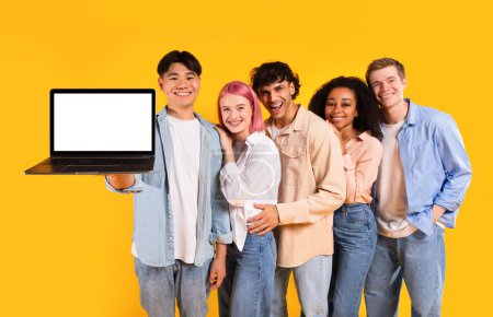 Photo for Five multiracial friends holding laptop showing blank computer screen, recommending educational website standing over yellow studio background, mockup - Royalty Free Image