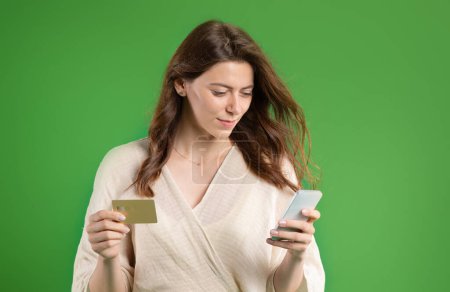 Photo for Cheerful young european lady in casual typing on smartphone, use credit card, enjoy online shopping, isolated on green studio background. Sale and app for banking and finance, ad and offer - Royalty Free Image