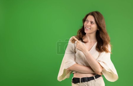Photo for Positive young european woman student in casual pointing fingers at free space, recommendation sale, isolated on green studio background. Ad and offer, professional advice - Royalty Free Image