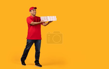 Photo for Pizza Delivery. Middle Eastern Courier Guy Holds Stack Of Pizzas Boxes, Delivering Food From Italian Restaurant Posing Over Yellow Studio Background. Full Length Shot, Empty Space For Text - Royalty Free Image