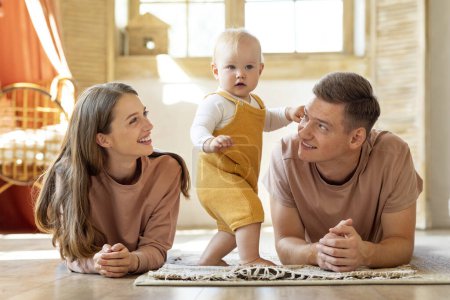 Photo for Happy Young Parents Looking At Their Adorable Little Baby While They Relaxing Together At Home, Smiling Mom And Dad Bonding With Infant Child While Resting On Floor In Living Room, Free Space - Royalty Free Image