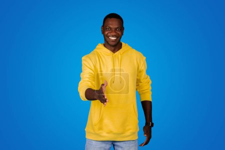 Photo for Happy young black guy shaking hands and saying hello, isolated on blue background, studio. human emotions, advertising and offer, lifestyle, hello - Royalty Free Image