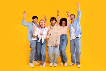 Photo for Winner concept. Group of diverse teen friends clenching fists, standing together over yellow background, excited for success with arms raised, celebrating victory - Royalty Free Image