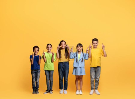 Photo for Adorable cheerful diverse school aged kids boys and girls in colorful casual outfits pointing at blank space for advertisement isolated on yellow background. Children recommending nice deal - Royalty Free Image