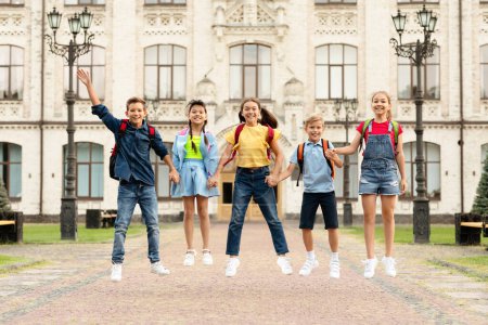 Photo for Happy Group Of Kids With Backpacks Holding Hands And Jumping Together Outdoors, Cheerful Multiethnic Boys And Girls Having Fun Against School Building, Ready For Lessons, Enjoying Education - Royalty Free Image