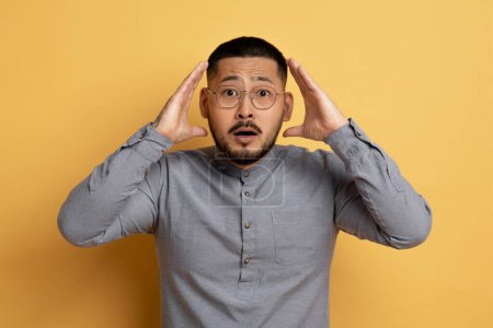 Photo for Portrait Of Shocked Young Asian Man Touching Head And Looking At Camera, Terrified Millennial Male In Eyeglasses Emotionally Reacting To Bad News, Standing Over Yellow Studio Background, Free Space - Royalty Free Image