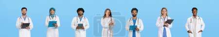 Photo for Smiling mature international professional doctors in white coats with tablets work, consulting, isolated on blue studio background, panorama. Medicine and health care in clinic - Royalty Free Image