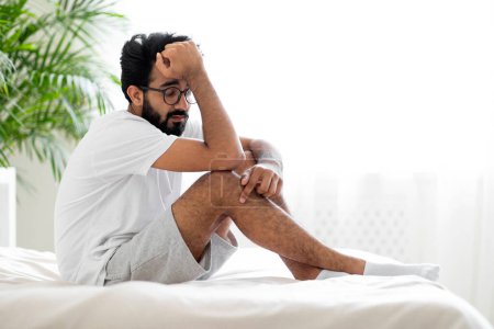 Photo for Sleepy Tired Young Indian Man Sitting On Bed At Home, Exhausted Millennial Eastern Guy Relaxing In Light Bedroom, Suffering Seasonal Depression Or Fatigue, Having Sleep Problems, Copy Space - Royalty Free Image