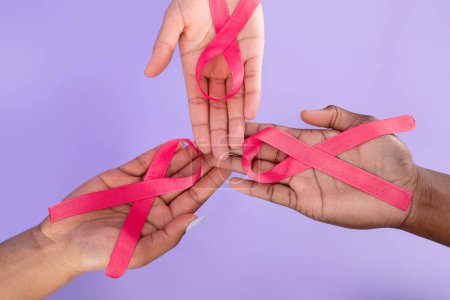 Téléchargez les photos : Breast Cancer Awareness Concept. Trois mains féminines tenant des rubans roses sur les paumes sur fond violet, gros plan, vue ci-dessus. Symboles d'oncologie pour bannière publicitaire - en image libre de droit