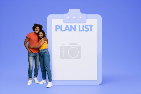 Photo for Smiling millennial black woman hugs man near big plan list with copy space, isolated on blue studio background. Future family planning, motivation, modern lifestyle, time management together - Royalty Free Image