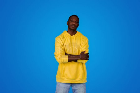 Photo for Serious strict confident handsome young black guy in hoodie with crossed arms on chest, look at camera, isolated on blue background, studio. Human emotions, ad and offer, lifestyle - Royalty Free Image