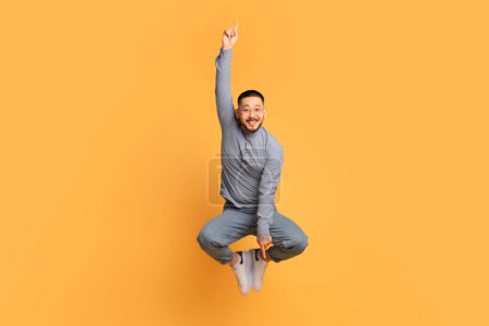 Photo for Check This. Cheerful Young Asian Man Pointing Up And Down While Jumping In Air, Positive Funny Millennial Guy Demonstrating Free Copy Space On Yellow Studio Background, Full Length Shot - Royalty Free Image