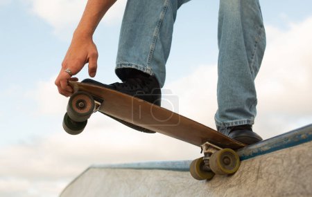 Photo for Unrecognizable young sports guy skateboarder riding at skate park with concrete walls, doing ramp tricks, posing on skateboard, closeup, cropped - Royalty Free Image