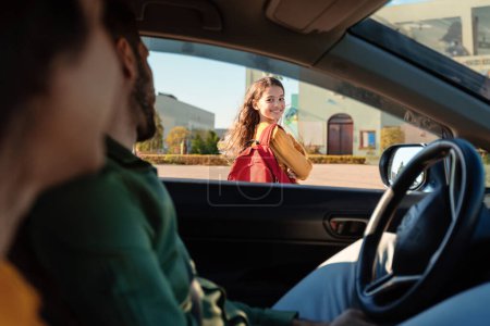 Photo for Mother and father dropping off daughter in front of school, schoolgirl turning back to parents sitting in car and smiling, view from inside auto - Royalty Free Image
