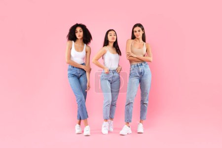 Photo for Three serious diverse women posing standing over pink studio background, full length shot of ladies friends trio looking at camera. Natural diverse female beauty - Royalty Free Image