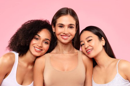 Téléchargez les photos : Portrait de jeunes amies multiraciales heureuses posant et souriant à la caméra, debout sur fond de studio rose. Diversité et beauté naturelle concept - en image libre de droit