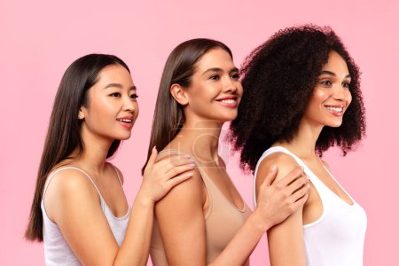 Téléchargez les photos : Belles dames multiethniques posant sur fond de studio rose, trois femmes millénaires regardant de côté et souriant, bannière, concept de diversité dans la beauté - en image libre de droit